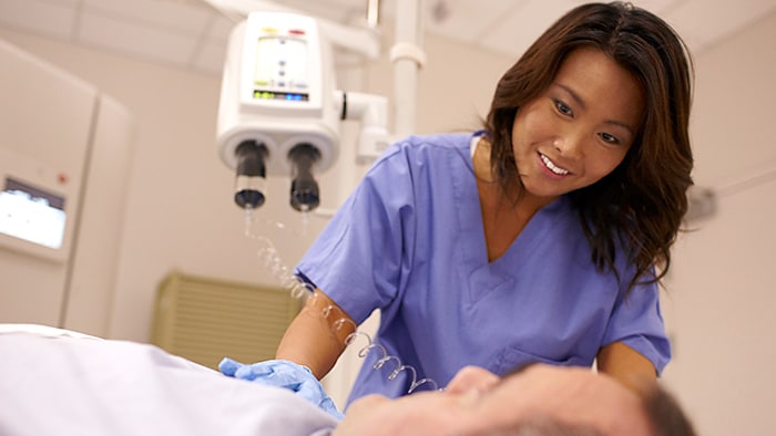A medical professional in scrubs smiles at a patient lying on a table
